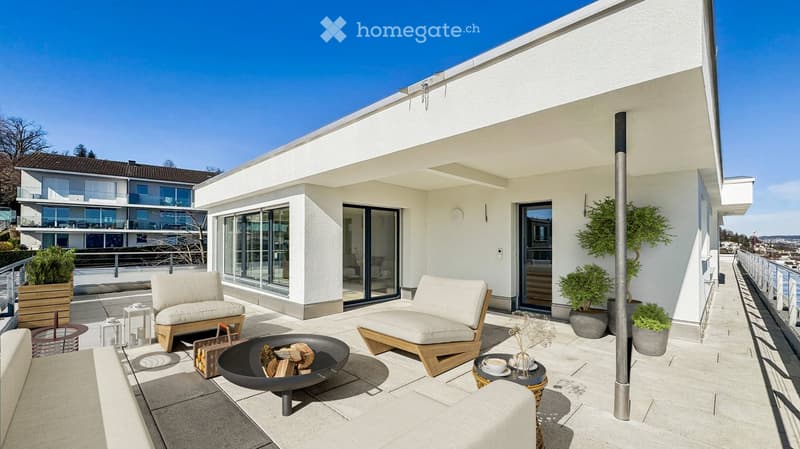 Modern rooftop terrace with white furniture, fire pit, small table with cups, and potted plants, overlooking a scenic view.