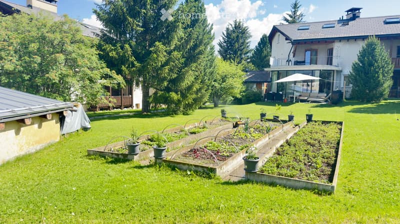 Well-maintained garden with raised vegetable beds, potted plants, and a modern house in the background.