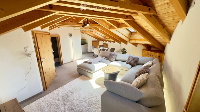 Cozy living room with exposed wooden beams, grey sectional sofa, coffee table, dining area with chairs and table, and small plant.