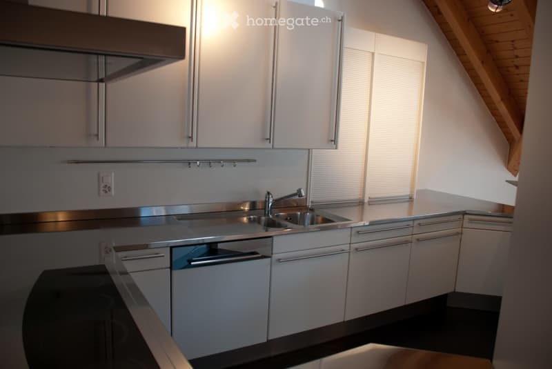 Modern kitchen with white cabinets, stainless steel sink, dishwasher, and stove. Features a sleek design with a black countertop and ample natural light from a window.