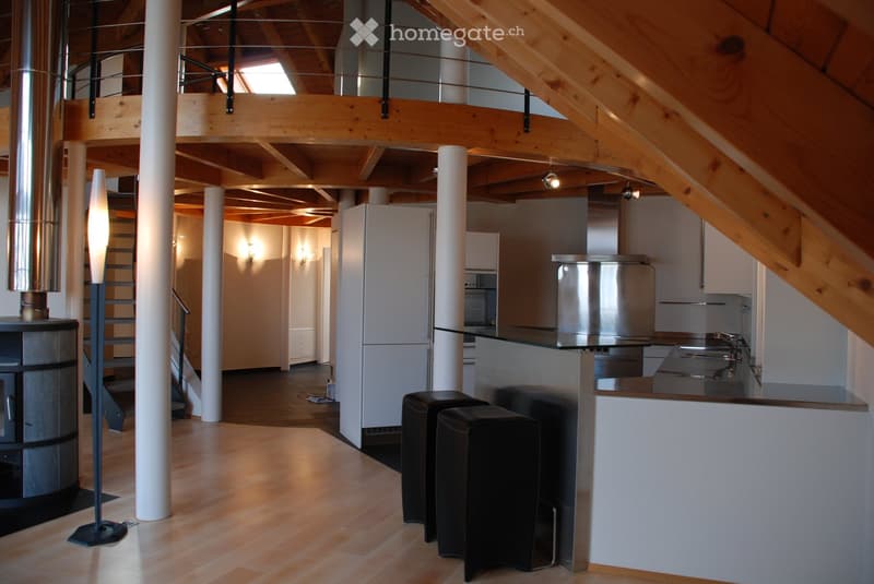 Open-plan living and kitchen area with wooden flooring, white cabinets, stainless steel appliances, and a modern fireplace.