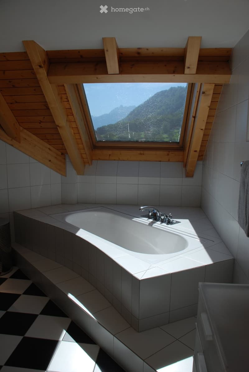 Modern bathroom with a large window offering a scenic mountain view, featuring a corner bathtub and sleek fixtures.
