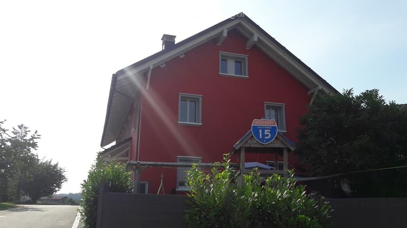 Red two-story house with white trim, multiple windows, and a small porch with a sign reading "Interstate California 15".