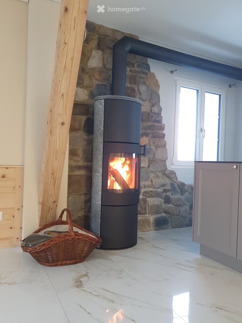 Modern room with a wood stove burning, stone wall, white tiled floor, and a wicker basket nearby.