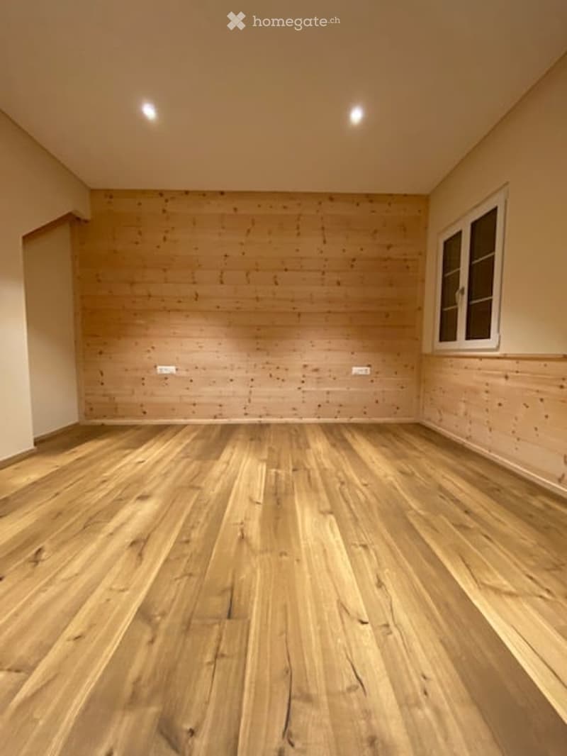Empty room with wooden flooring and light-colored walls, featuring a single window with white frame and built-in lighting.