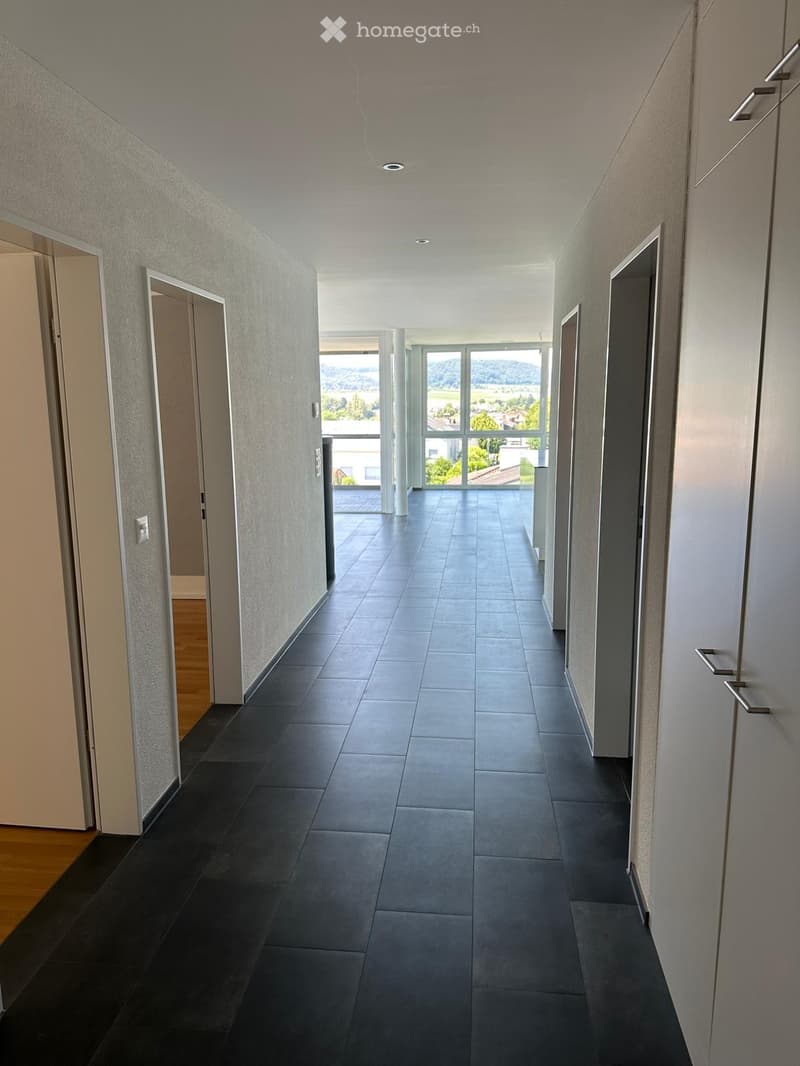 Modern hallway with tiled floor, grey walls, and large windows at the end offering a scenic view.