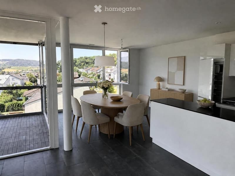 Modern open-plan kitchen and dining area with large windows offering a scenic view, featuring a round dining table with six chairs, a kitchen counter, and various decorative items.
