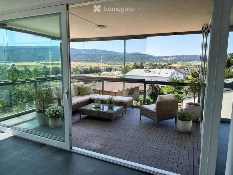 Balcony with a panoramic view, featuring a sofa, coffee table, chair, and potted plants.
