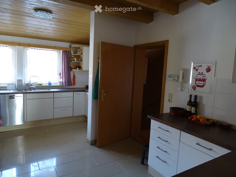 Bright kitchen with white cabinets, dark countertop, sink, dishwasher, and fruit bowl on the counter. Wooden ceiling beams and a window with curtains.