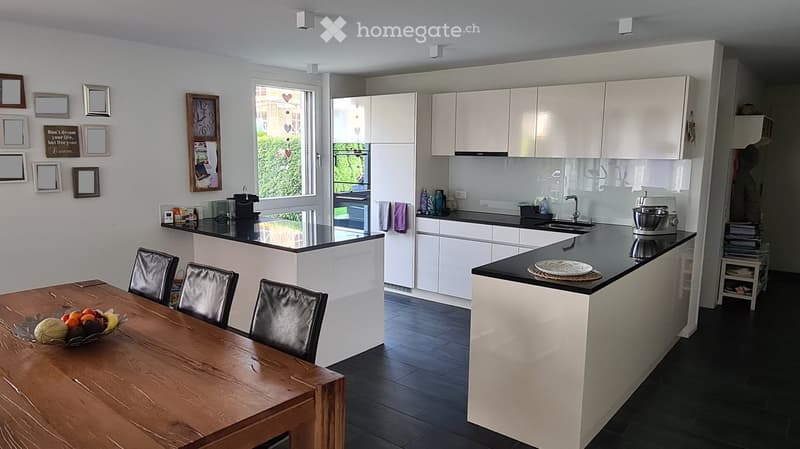 Modern kitchen with white cabinets, black countertops, and a wooden dining table with chairs. The kitchen features a sink, faucet, and various appliances.