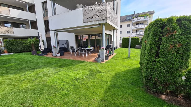 Well-maintained garden with a wooden deck, outdoor furniture, grill, and potted plants.