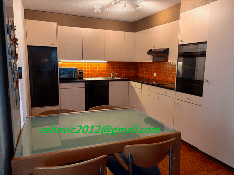 Modern kitchen with white cabinets, black appliances, and a glass dining table with chairs.