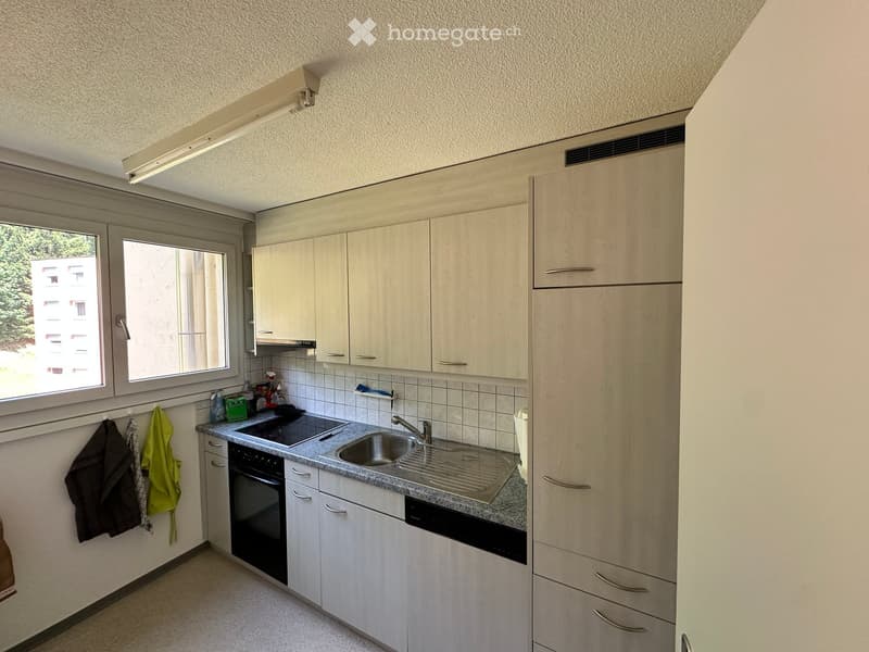 Modern kitchen with light wood cabinets, stainless steel sink, oven, and dishwasher. Countertop has a few cleaning supplies and a dish rack.