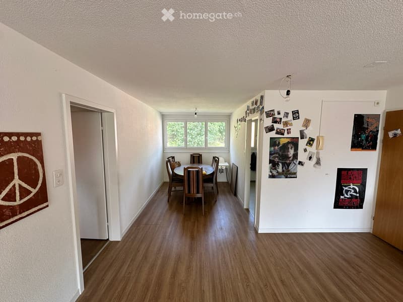 Dining area with wooden floor, dining table, chairs, posters, and a peace sign tapestry on the wall.