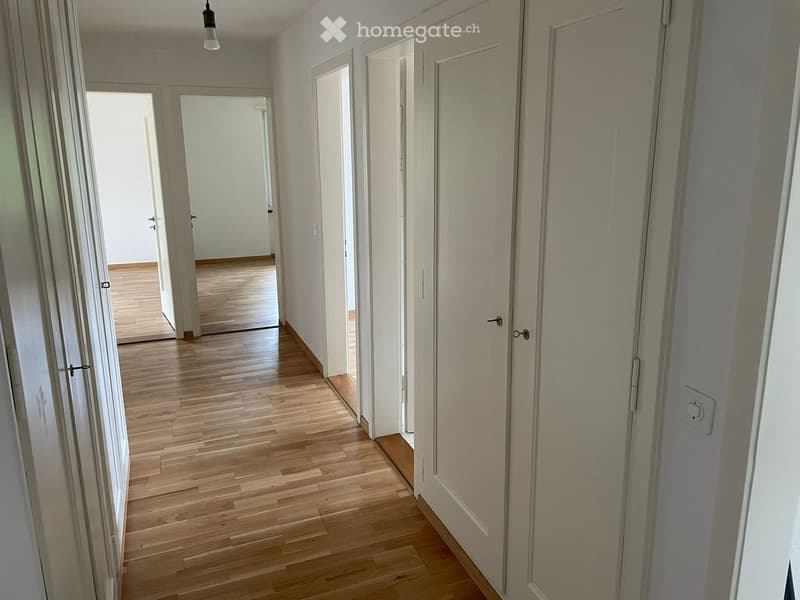 Empty hallway with wooden flooring, white walls, and multiple doors leading to other rooms.