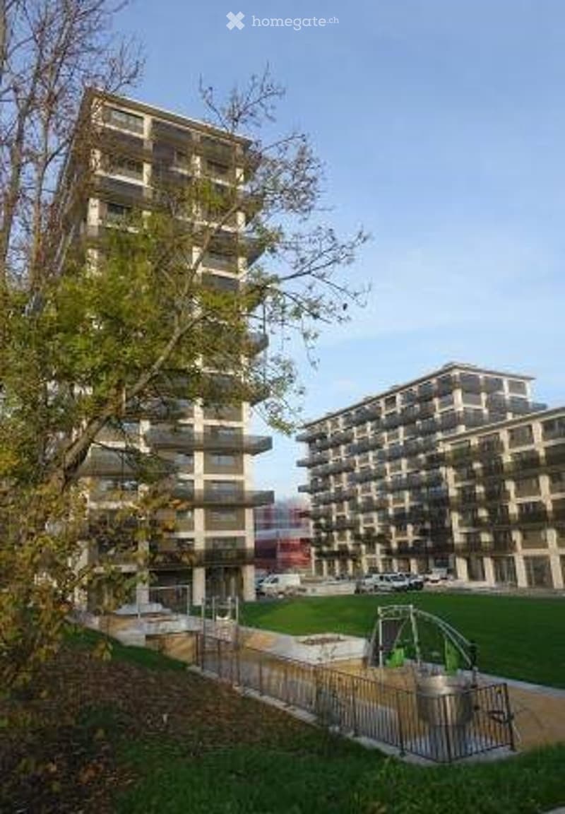 Modern multi-story residential building with balconies, surrounded by green space and playground area.