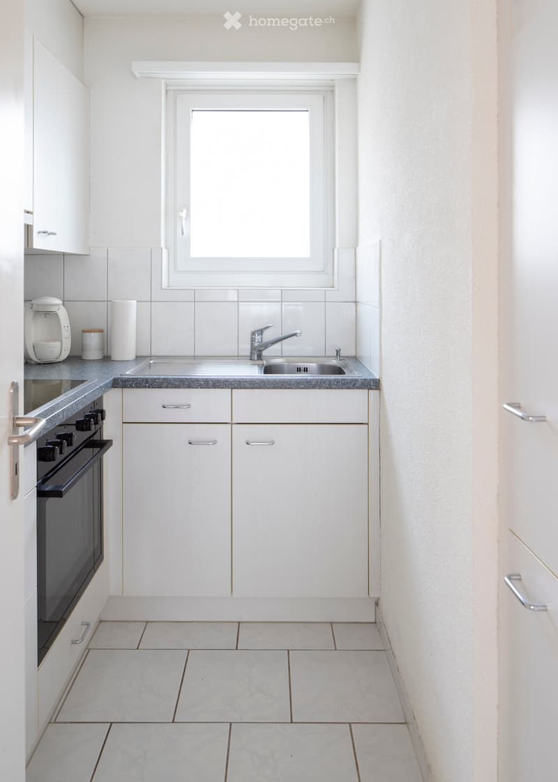Modern kitchen with white cabinets, tiled backsplash, granite countertop, stainless steel sink, and built-in oven.