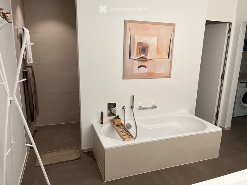 Modern bathroom with a large bathtub, towel rack, shower hose, handrail, and a painting on the wall.