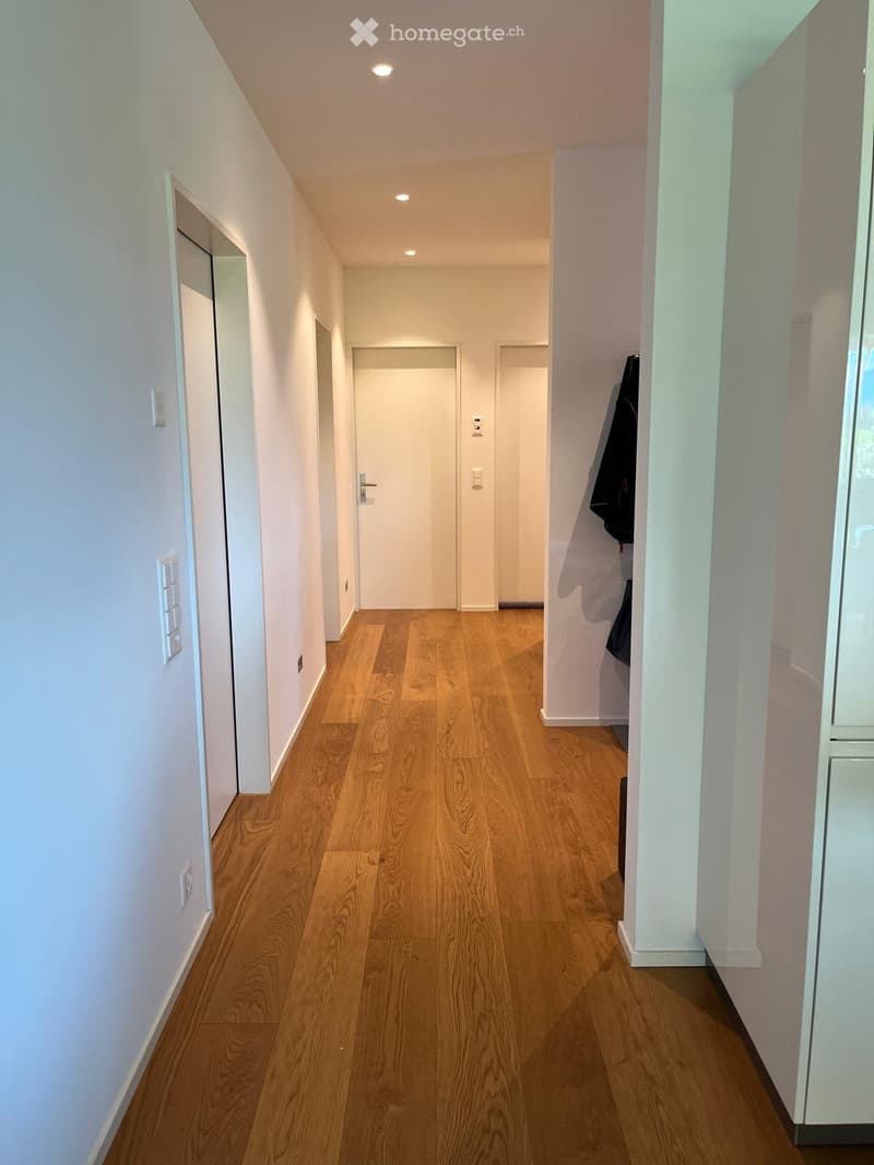 A clean, well-lit hallway with wooden flooring, white walls, and several doors leading to other rooms.