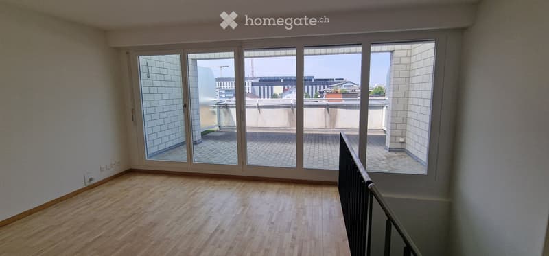 Empty room with wooden flooring, large glass sliding doors leading to a balcony, and white tiled walls.