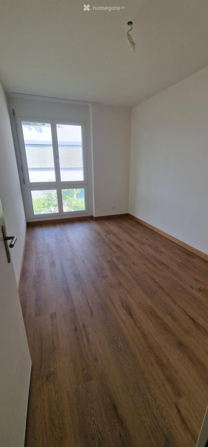 Empty room with wooden flooring, white walls, and large windows with blinds. No furniture or equipment present.