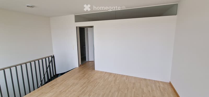 Empty hallway with wooden flooring, white walls, and a staircase leading to another room.