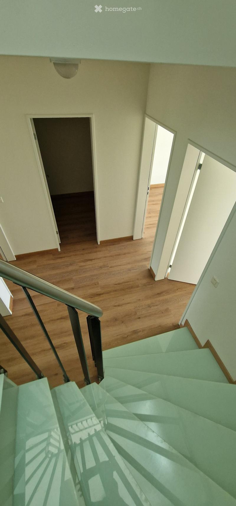 Spiral staircase with wooden steps and metal railing, leading to open doorways on the upper level.