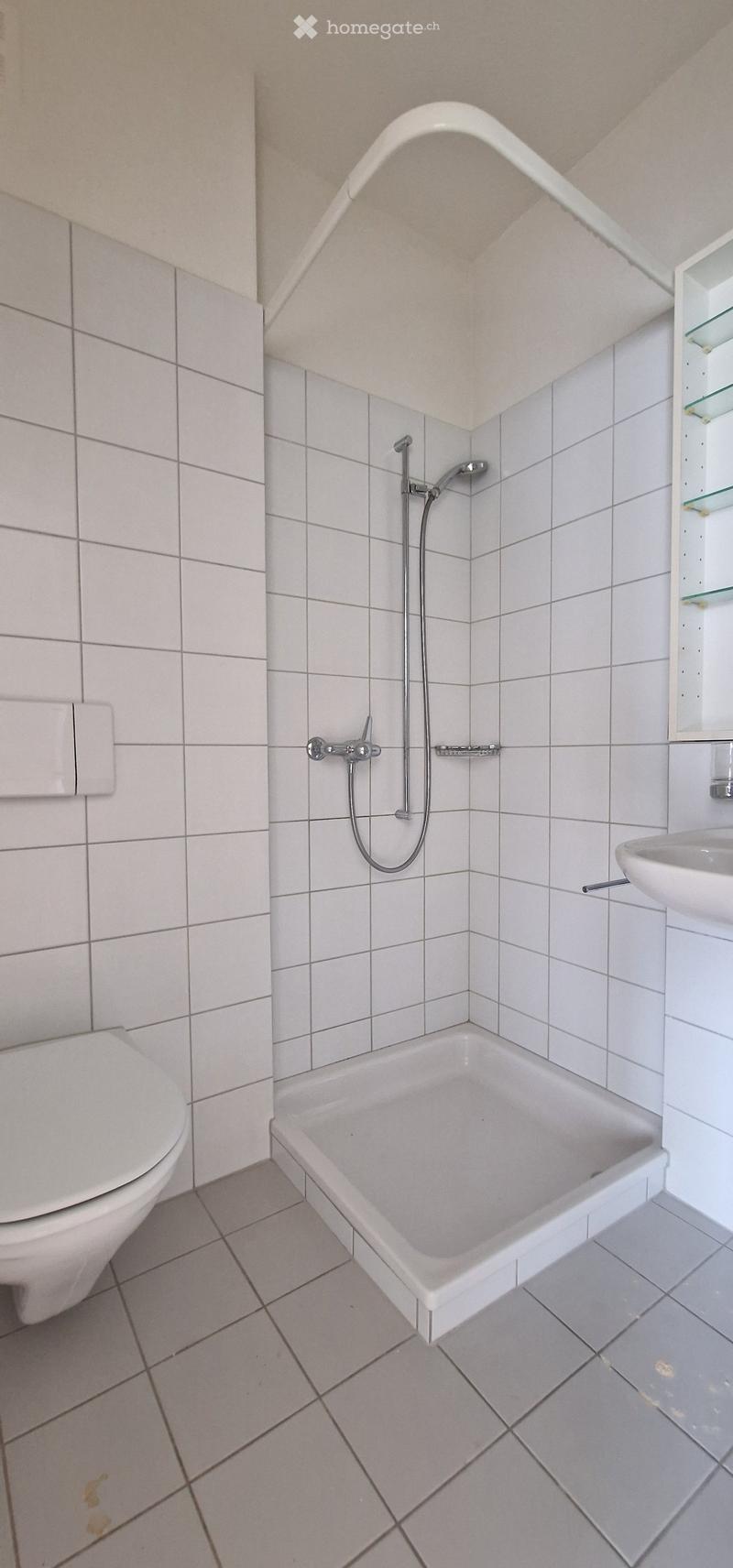 Bathroom with white tiled walls and floor, featuring a bathtub, toilet, sink, and showerhead.