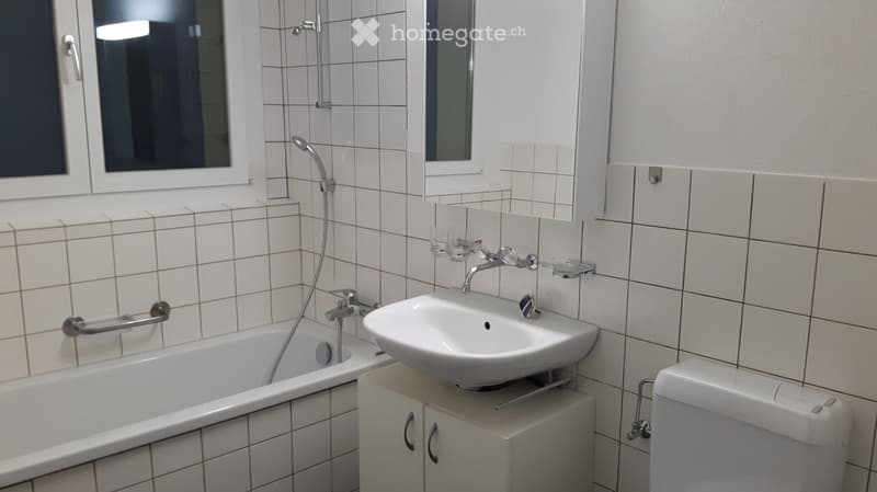 Modern bathroom with white tiled walls, a bathtub, a sink with a modern faucet, a toilet, and a mirror above the sink.