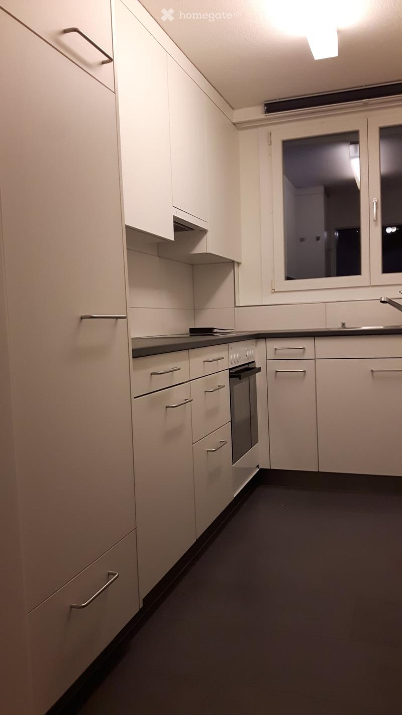 Modern kitchen with white cabinets, stainless steel handles, and a black countertop. Features an oven and a sink.