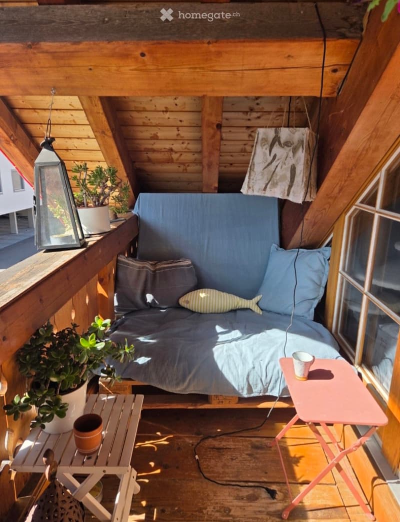 Cozy wooden balcony with a small sofa, two side tables, potted plants, and a lantern.