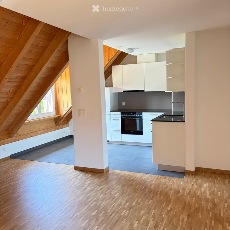 Modern kitchen with white cabinets, stainless steel appliances, and wooden flooring. The space features an open layout with a wooden ceiling and large windows.