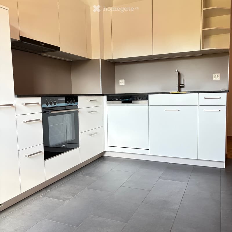 Modern kitchen with white cabinets, stainless steel appliances, and grey tiled flooring.
