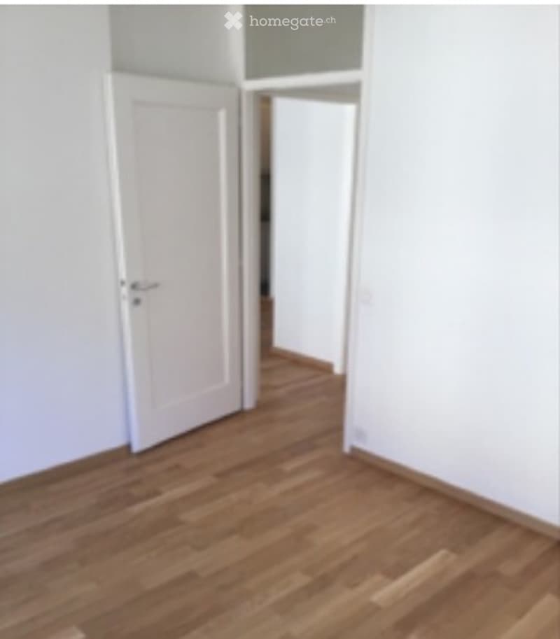 Empty room with wooden flooring and white walls, featuring two open doors leading to adjacent spaces.