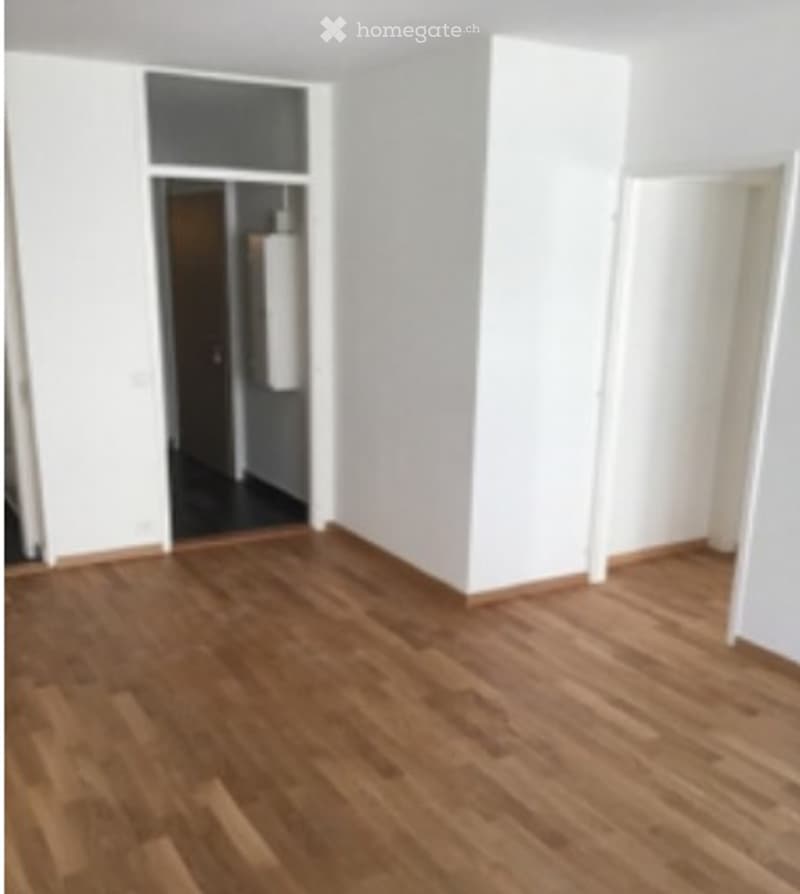 Empty room with wooden flooring and white walls, featuring an open doorway leading to another room.