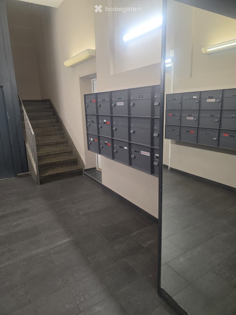 Hallway with dark tiled floor, beige walls, staircase with metal railing, and mailboxes mounted on the wall.