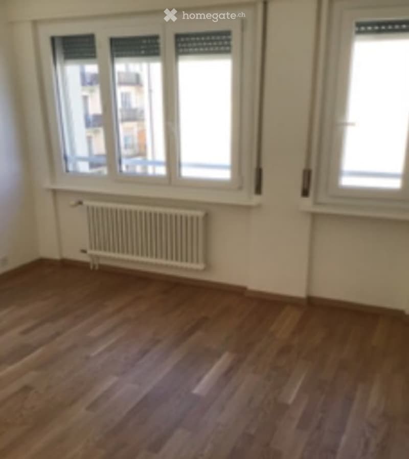 Empty room with wooden flooring, white walls, and a radiator under a window. No furniture or equipment present.