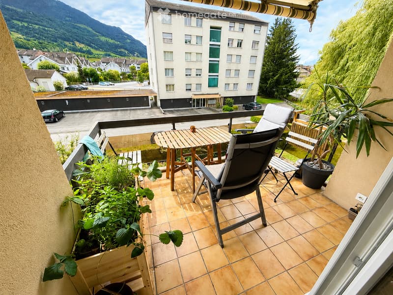 Balcony with wooden table, chairs, potted plants, and scenic mountain view.