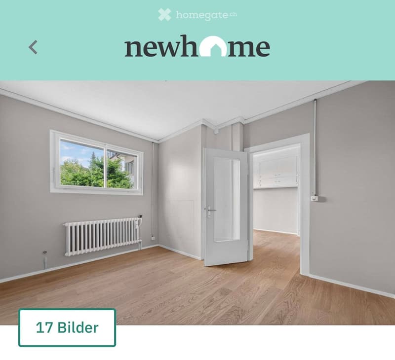 Empty room with wooden flooring, grey walls, a window with a view of greenery, a radiator, and an open door leading to another space.