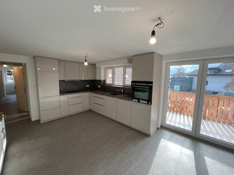Modern kitchen, white cabinets, granite countertops, stainless steel appliances, grey tiled floor, sliding glass doors to balcony, overhead lighting