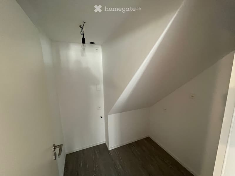 Empty room with a white door, white walls, wooden floor, two power outlets, and a ceiling lamp.