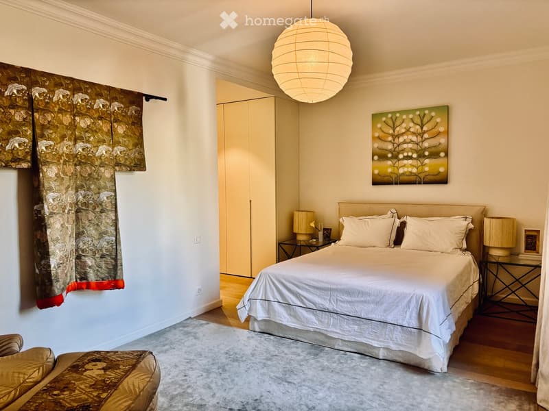 Elegant bedroom with a large bed, nightstands, lamps, a patterned chair, and a painting on the wall.