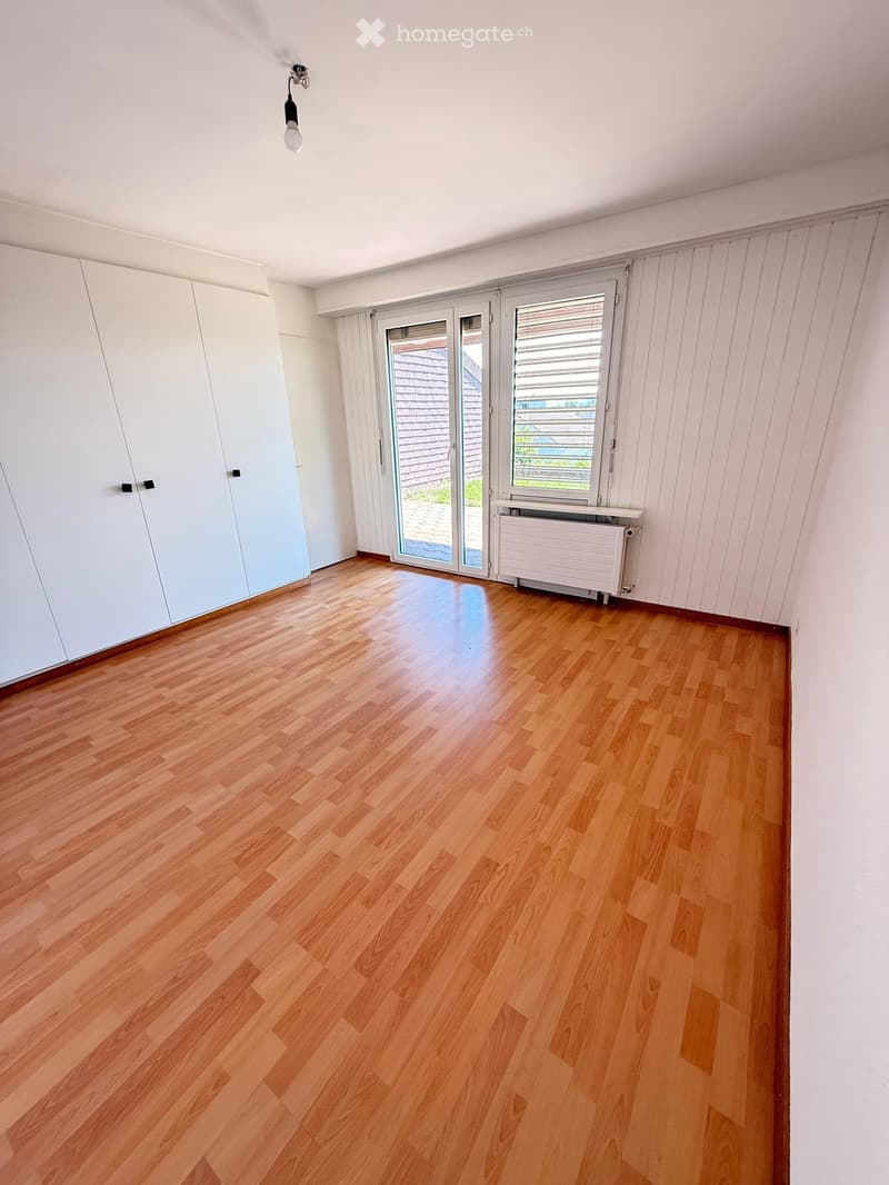 Empty room with wooden flooring, white walls, large sliding glass door, and built-in white closet.