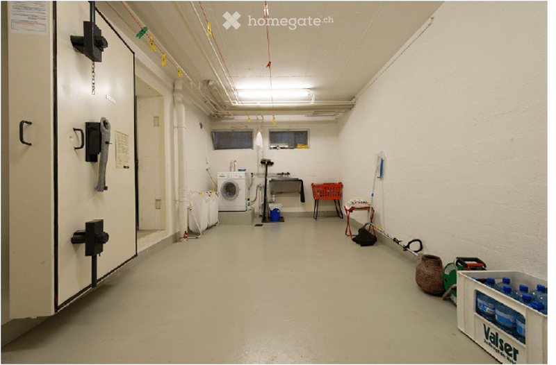 Empty utility room with white walls, concrete floor, washing machine, and storage items.