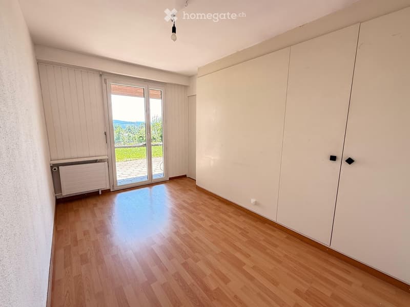Empty room with wooden flooring, white walls, large sliding glass door leading to a balcony, radiator, and built-in closet.