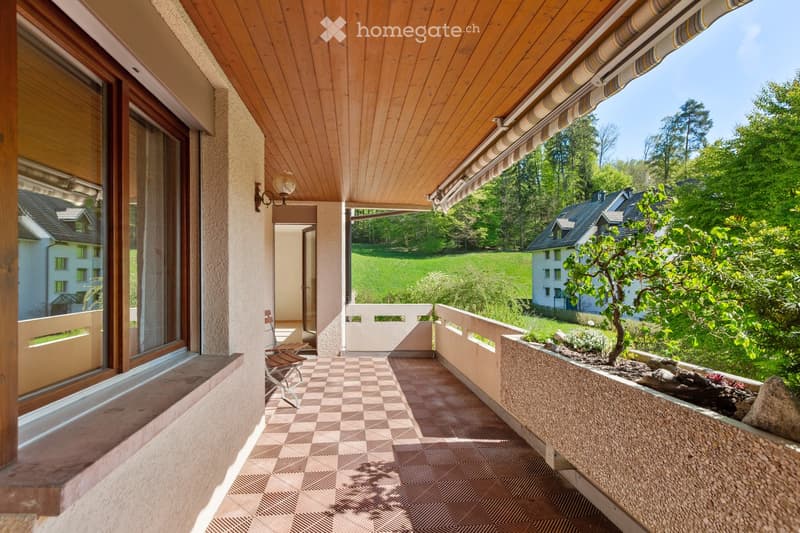 Balcony with wooden ceiling, checkered tile floor, and scenic view of a green landscape and neighboring houses.