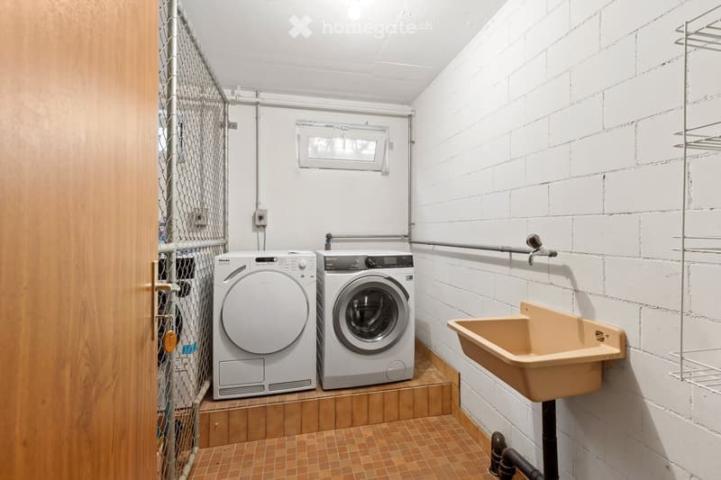 A small bathroom with a washing machine, dishwasher, and a sink. The walls are white brick, and the floor is tiled.