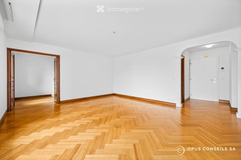 Empty room with white walls, wooden herringbone flooring, and two doors.
