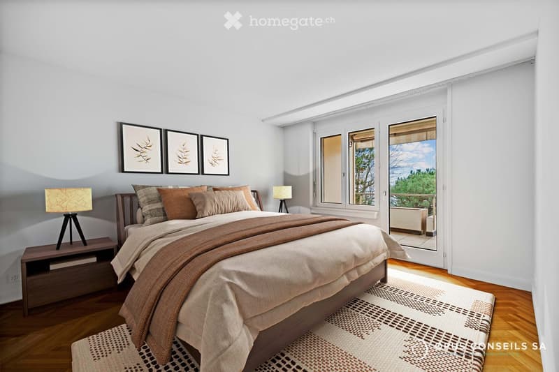 Bright bedroom with wooden flooring, large windows, and a balcony view. Features a bed with pillows and blankets, a nightstand with a lamp, and a patterned rug.