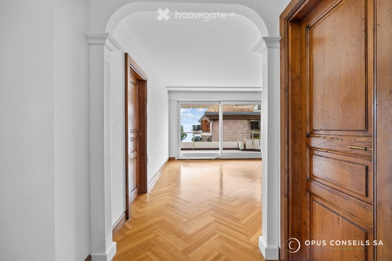 Elegant hallway with herringbone wooden flooring, white walls, and arched doorways leading to a balcony area with outdoor seating.